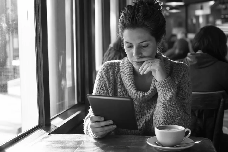 Person reading on a tablet with a coffee at a table