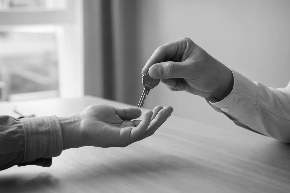 One person handing a key to another across a desk